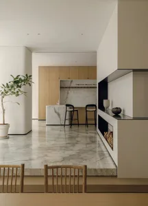 Modern kitchen with white marble countertops, a fireplace, and a dining table, creating a warm and inviting atmosphere
