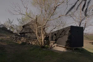 A black house with a stone wall surrounded by trees, situated on a hill, creating a nostalgic atmosphere