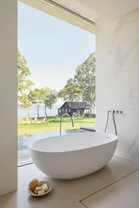 A modern bathroom with a large white bathtub in front of a window, surrounded by natural light