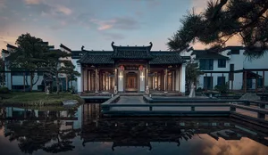 A large ornate building with a Chinese architectural style, featuring a pagoda-like structure and a stone roof, surrounded by a serene pond