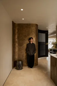 A calm and inviting living space with a brown wall, a dining table, and a chair, with a man standing in the center of the room