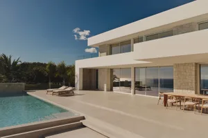 A modern house with a clean and minimalist design, featuring a lot of glass and concrete, surrounded by a patio area with a pool and outdoor furniture