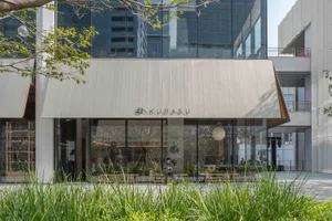 A restaurant building with a large window, a sign, and a tree outside, set in a neutral color palette with natural light pouring in