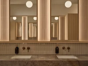 A modern bathroom with two sinks, metal sinks, a wooden countertop, and a tile floor, well-lit and clean
