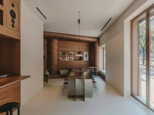 A modern living room with a wooden floor, a dining table, kitchen counter, couch, chair, and bookshelf, well-lit and inviting