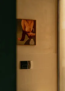 A calm and inviting bathroom with a woman's picture on the wall, a tiled floor, and a white wall, with a vase on display