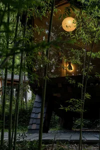 Cozy living space with a bamboo-style structure, surrounded by trees, featuring a dining table and chairs, with natural light streaming in through the windows