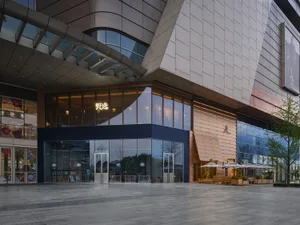 A modern building with a large glass window and a large door, surrounded by concrete and natural light