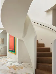 A modern staircase with white and wooden steps in a residential hallway, lit by natural sunlight from a window