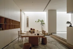A well-lit dining room with a wooden table and chairs, surrounded by a potted plant, creating a warm and inviting atmosphere