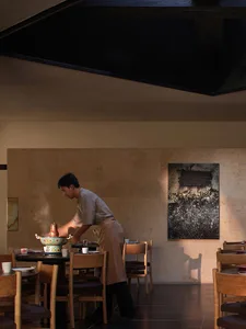 A modern restaurant dining area with wooden tables and chairs, well-lit by natural light and warm ambiance