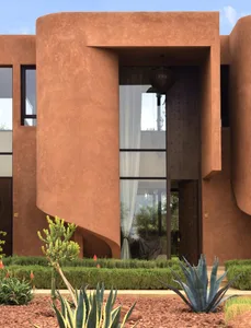 A modern building with a curved structure and large window, featuring a brick exterior and a potted plant in front