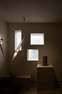 Small dimly lit room with a white wall, a window, two hanging lights, a table with a vase, and a potted plant near the left side