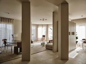 A living room with a couch, chair, and dining table, featuring a large window that lets in natural light, creating a bright and welcoming atmosphere