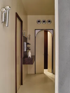 A modern bathroom with a sink, mirror, and door, featuring predominantly white surfaces and natural light