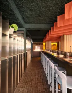 A dimly lit restaurant interior with a long dining table, chairs, and potted plants, set in a modern and inviting space