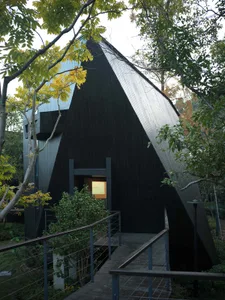 A black and white photograph of a modern house with a triangular shape, surrounded by trees, showcasing its architectural features and natural environment