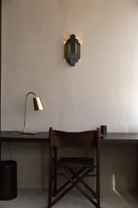 A dimly lit room with a wooden chair and desk setup, featuring a brown leather-like chair and a lamp on the left side of the desk