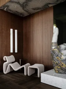 A modern room with a wooden wall, a white floor, and a large statue of a hand as the main focal point, accompanied by two chairs, a couch, and a vase, in a dimly lit space