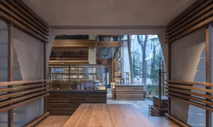 A warm and inviting restaurant interior with a large wooden dining table, wooden chairs, and a wooden counter, surrounded by natural lighting