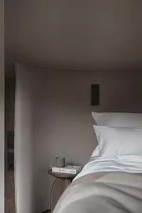 Cozy bedroom with a wooden bed, nightstand, and floor, dimly lit with a lamp and a book on the nightstand