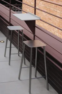 Dining area with a white metal counter, metal stools, and a brick wall, lit by natural light