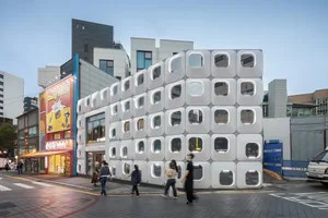 A modern building with white blocks and numerous windows, set in a bustling city street with people walking by