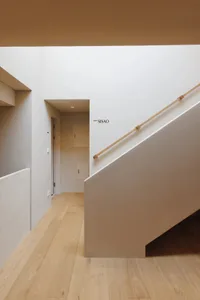 A modern staircase in a hallway with a white wall, surrounded by natural light from a window