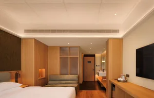 Cozy bedroom with a bed, couch, and mirror, surrounded by wooden furniture and a wooden floor, in a well-lit space