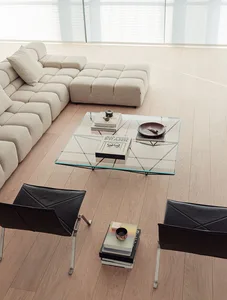 A living room with a large couch, glass coffee table, and bookshelf, featuring a clean and modern appearance with a wooden floor and predominantly white furniture