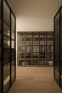A dimly lit hallway with a wooden floor and white walls, lined with open glass doors revealing a closet with clothes and a cozy atmosphere