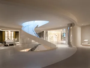 A modern, white, circular building with a glass spiral staircase, blending living and dining areas, with a dining table and sleek, open design