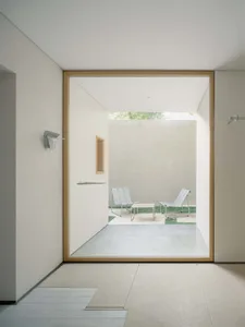 A well-lit outdoor patio area with a bench and chair, both made of wood, near a doorway leading to a room