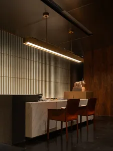 Modern kitchen with a dining table, chairs, and a vase, featuring marble countertops, wood flooring, and a dimly lit atmosphere