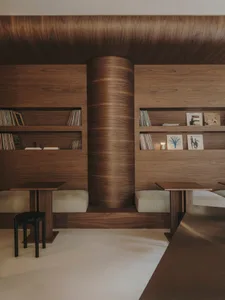 A warm and inviting room with wooden walls and floors, featuring a dining table, chairs, bookshelf, and couch, with a comfortable and relaxing atmosphere