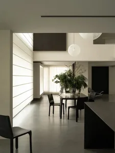 A modern living space with a large dining table, chairs, and potted plant, surrounded by furniture and well-lit for a bright atmosphere
