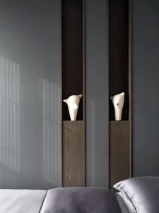 A cozy bedroom with a wooden shelf and two vases, a bed visible in the background