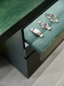 A wooden desk with a drawer and a display of silver and blue watches on a well-lit living space