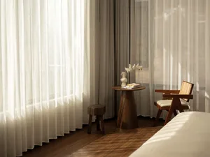 A well-lit bedroom with a wooden floor, a bed, a chair, and a table, creating a comfortable and inviting atmosphere