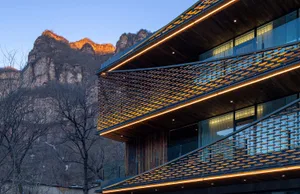 A modern building with a glass facade and wooden accents, situated in front of a mountain, with natural light and a sense of luxury and tranquility
