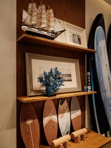Cozy living space with a wooden shelf displaying surfboards, framed pictures, and a plant, suggesting a relaxed coastal atmosphere