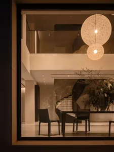 A well-lit modern dining room with a glass table, chairs, and a potted plant, surrounded by natural light from the windows