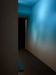 Narrow hallway with a blue wall, black curtain, and blue carpet, lit by dim lighting