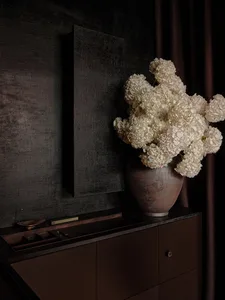 一間溫馨的生活空間，牆面為黑色，桌面為棕色，桌上有一個白色花瓶裝著白色花