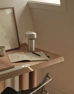 A wooden desk with a cup of coffee, a book, and a pen in a cozy room with a window and a picture on the wall