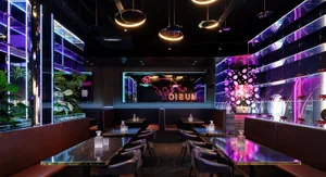 A modern restaurant interior with purple lighting, wood, and glass, featuring dining tables and chairs in a well-lit and inviting space