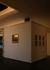 Dimly lit modern room with a concrete wall and multiple framed pictures on the wall