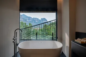 A serene bathroom with a white bathtub, black railing, and a large window offering a breathtaking mountain view