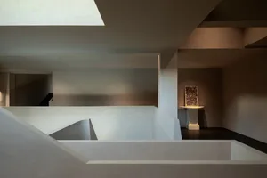 A modern art gallery with a white wall, a large window, and a painting displayed near the center of the wall, with natural light streaming in