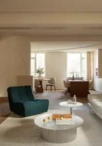 Cozy modern living space with a blue couch, dining table, and kitchen area, featuring natural light, a potted plant, and wine glasses